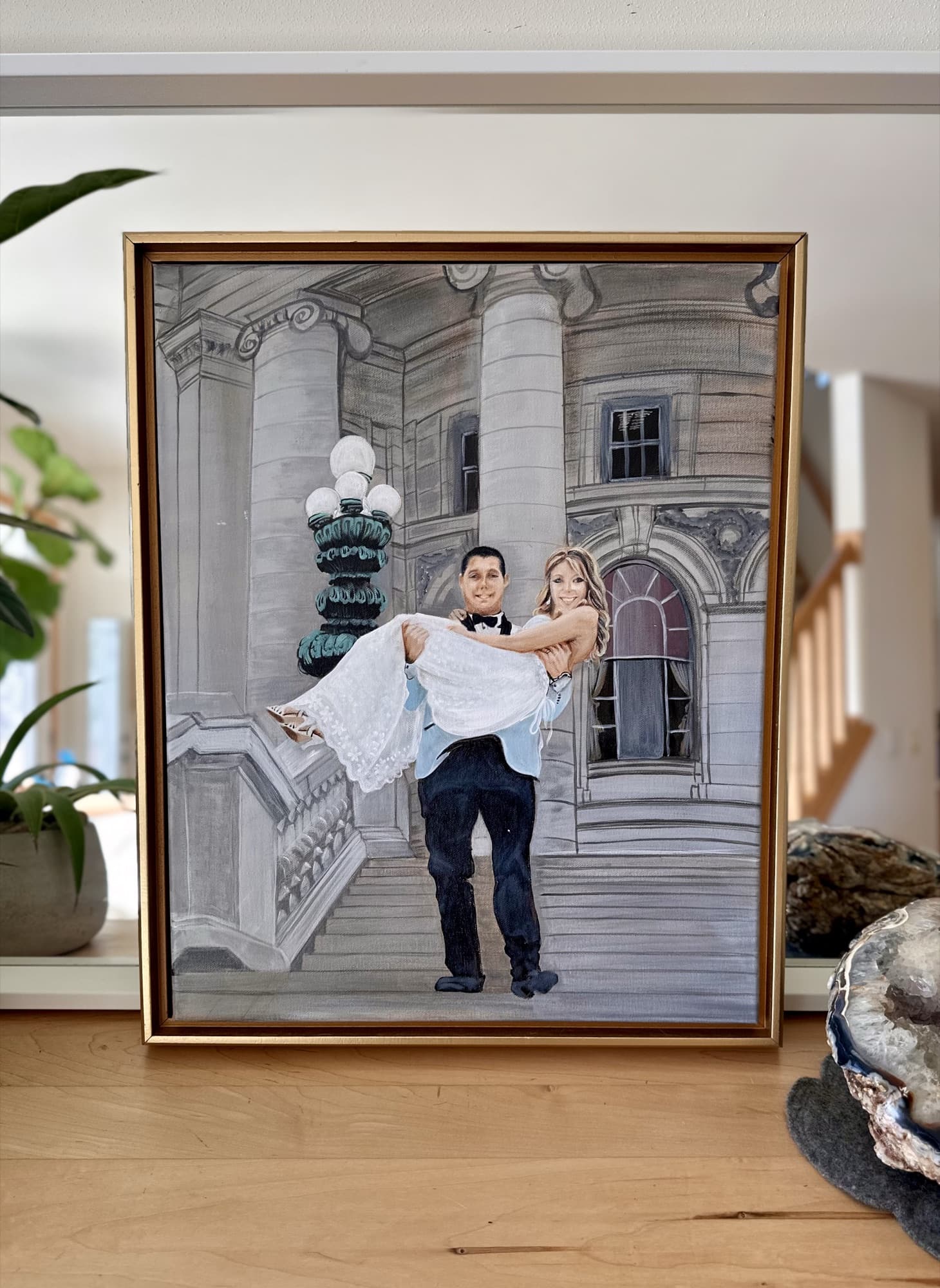 Capitol steps wedding painting on a wood console, with a houseplant and decorative shell beside the frame