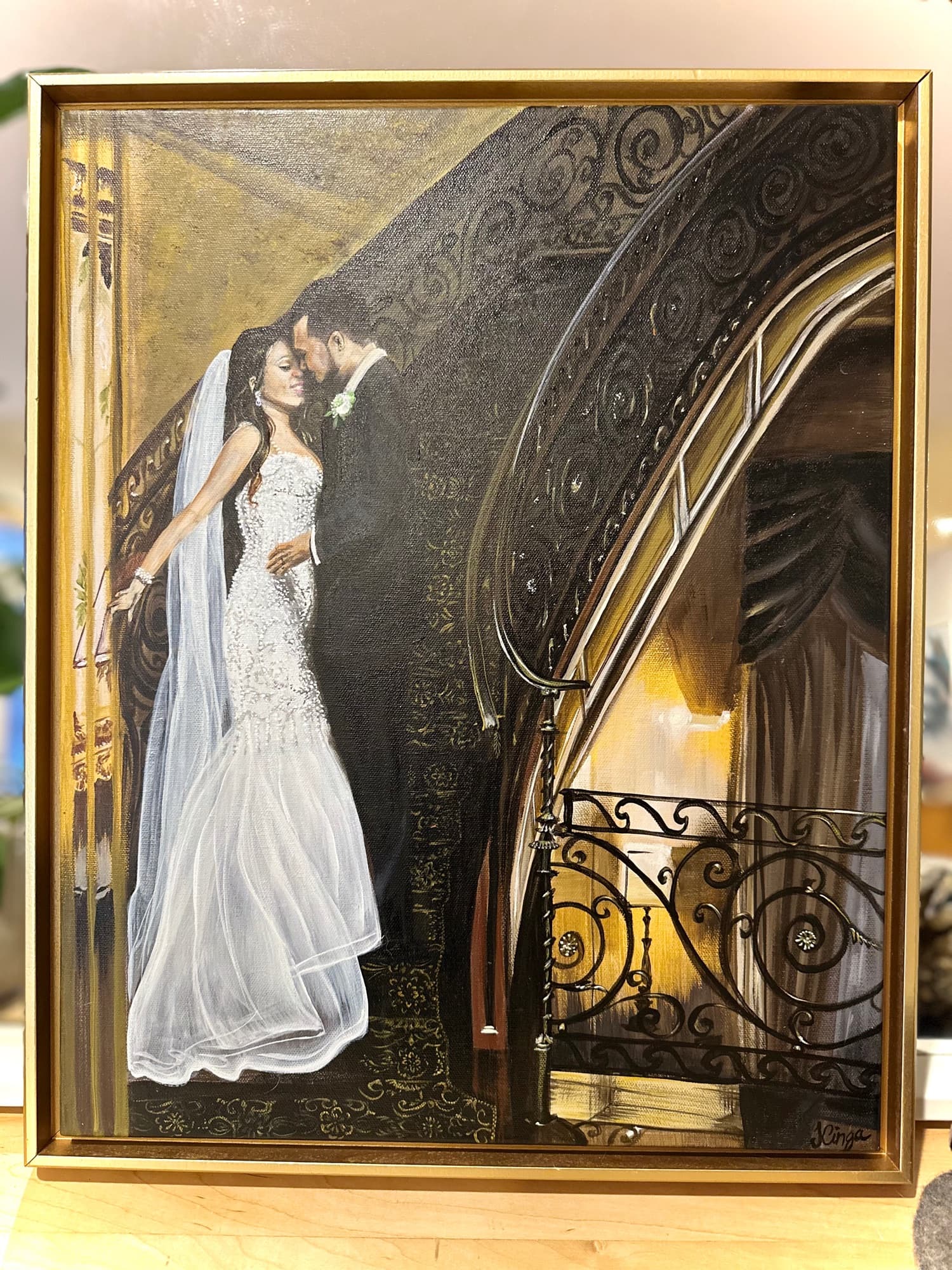 Framed live wedding painting of a bride and groom embracing at the foot of an ornate wrought-iron staircase